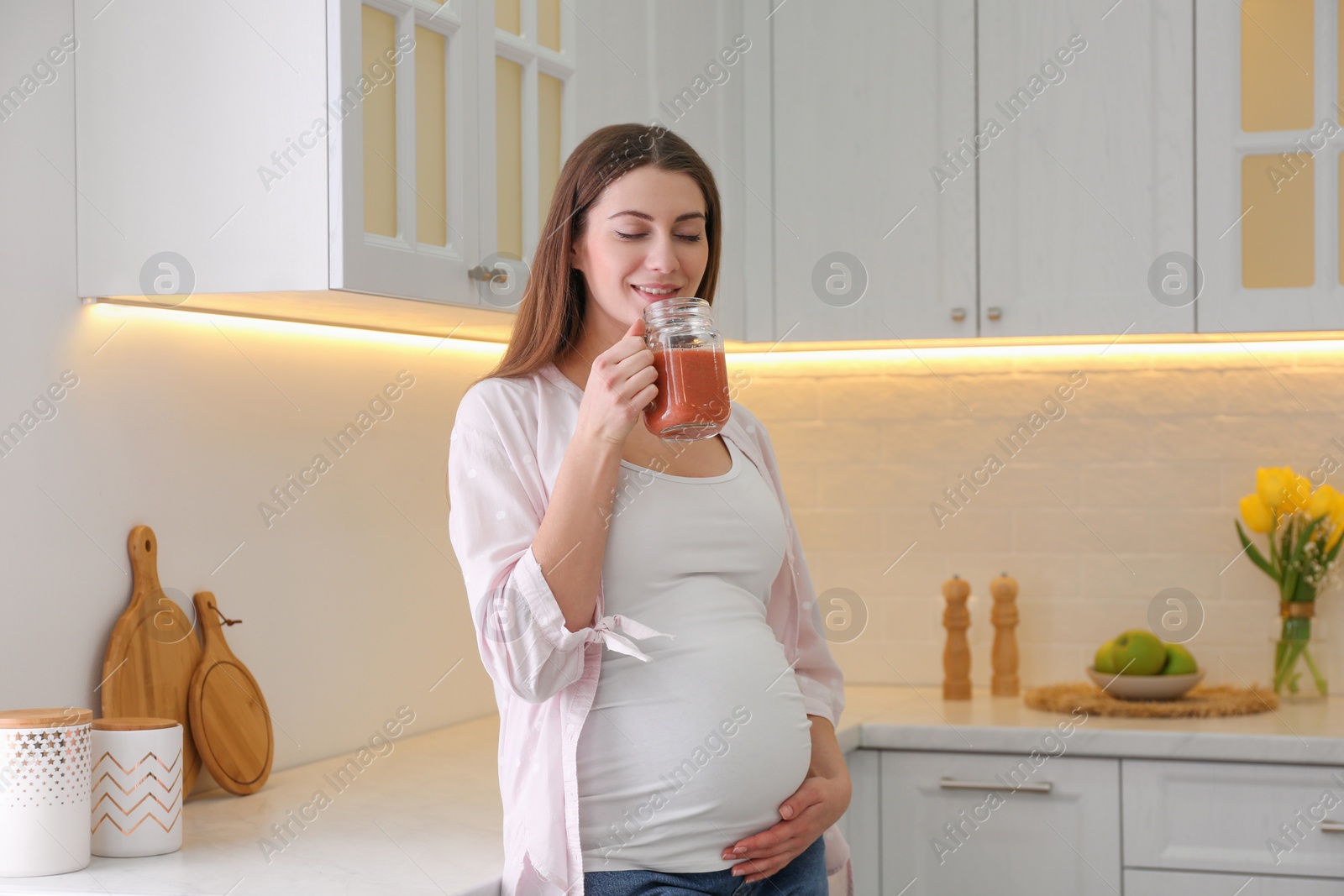 Photo of Young pregnant woman with smoothie in kitchen. Healthy eating