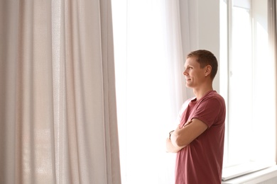 Photo of Mature man near window with open curtains at home. Space for text