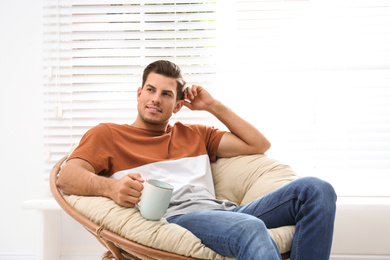 Attractive man relaxing in papasan chair near window at home