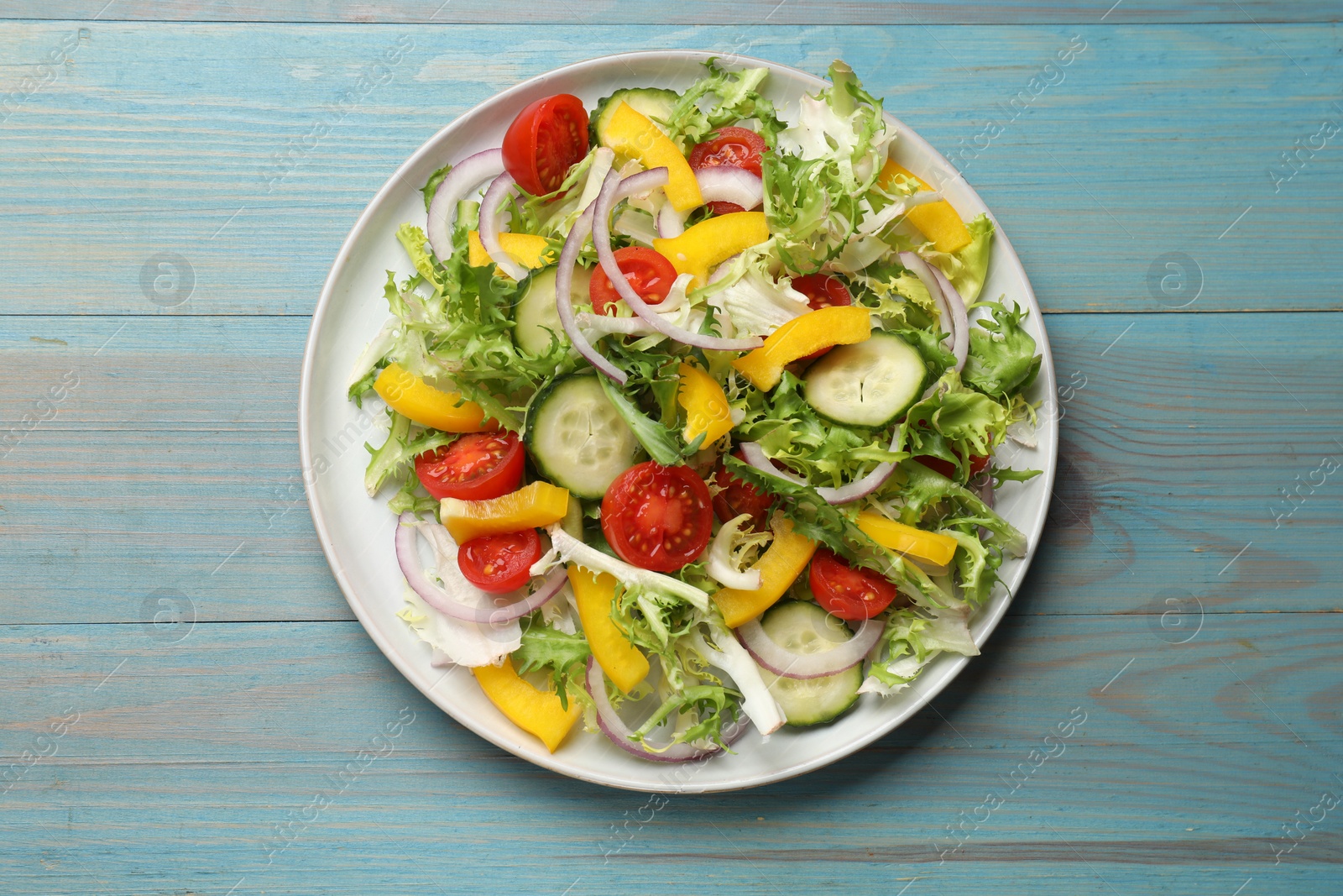 Photo of Tasty fresh vegetarian salad on light blue wooden table, top view