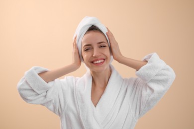 Beautiful young woman with hair wrapped in towel after washing on beige background