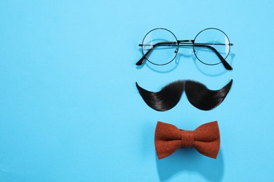 Photo of Artificial moustache, bowtie and glasses on light blue background, flat lay. Space for text