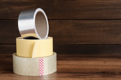 Photo of Three different rolls of adhesive tape on wooden table. Space for text