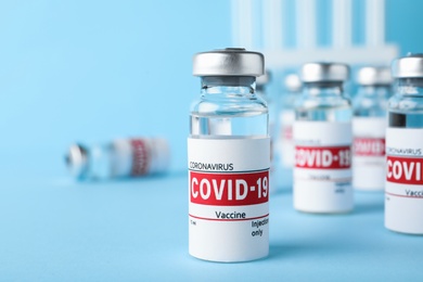 Photo of Glass vials with COVID-19 vaccine on light blue table