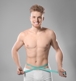 Photo of Portrait of young man with measuring tape showing his slim body on grey background
