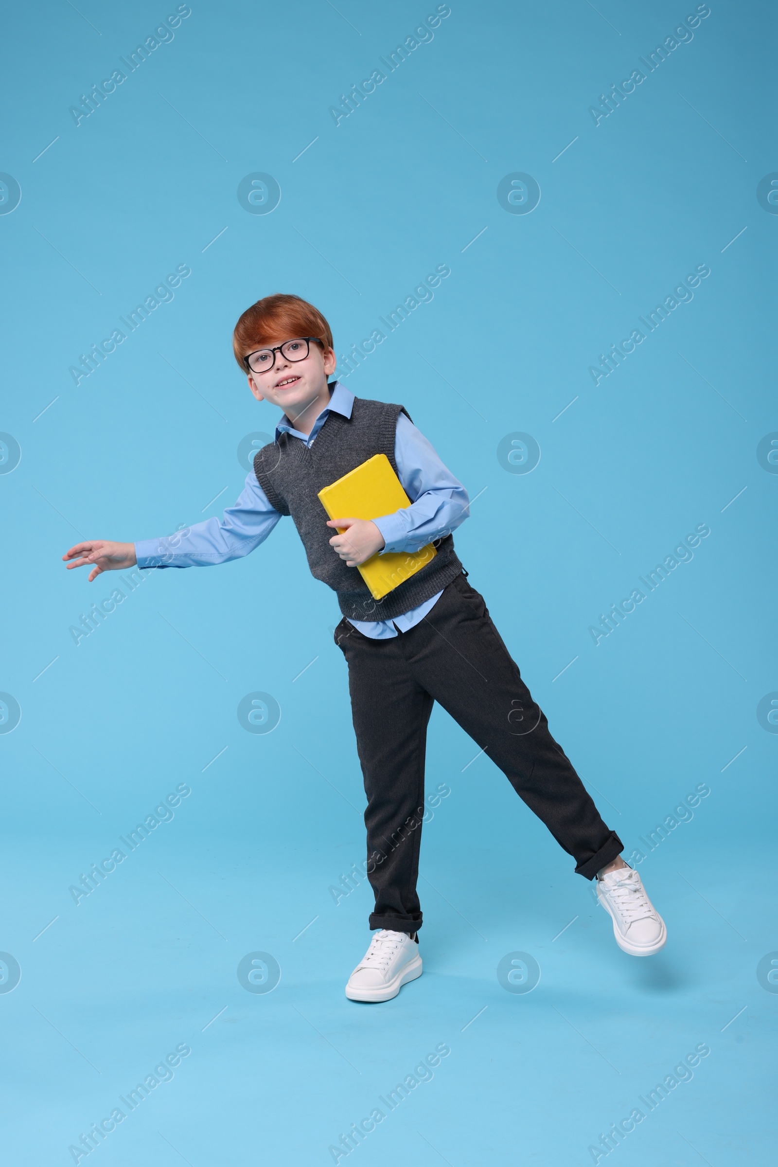 Photo of Smiling schoolboy in glasses with book on light blue background