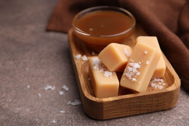 Yummy caramel candies, sauce and sea salt on brown table, closeup. Space for text