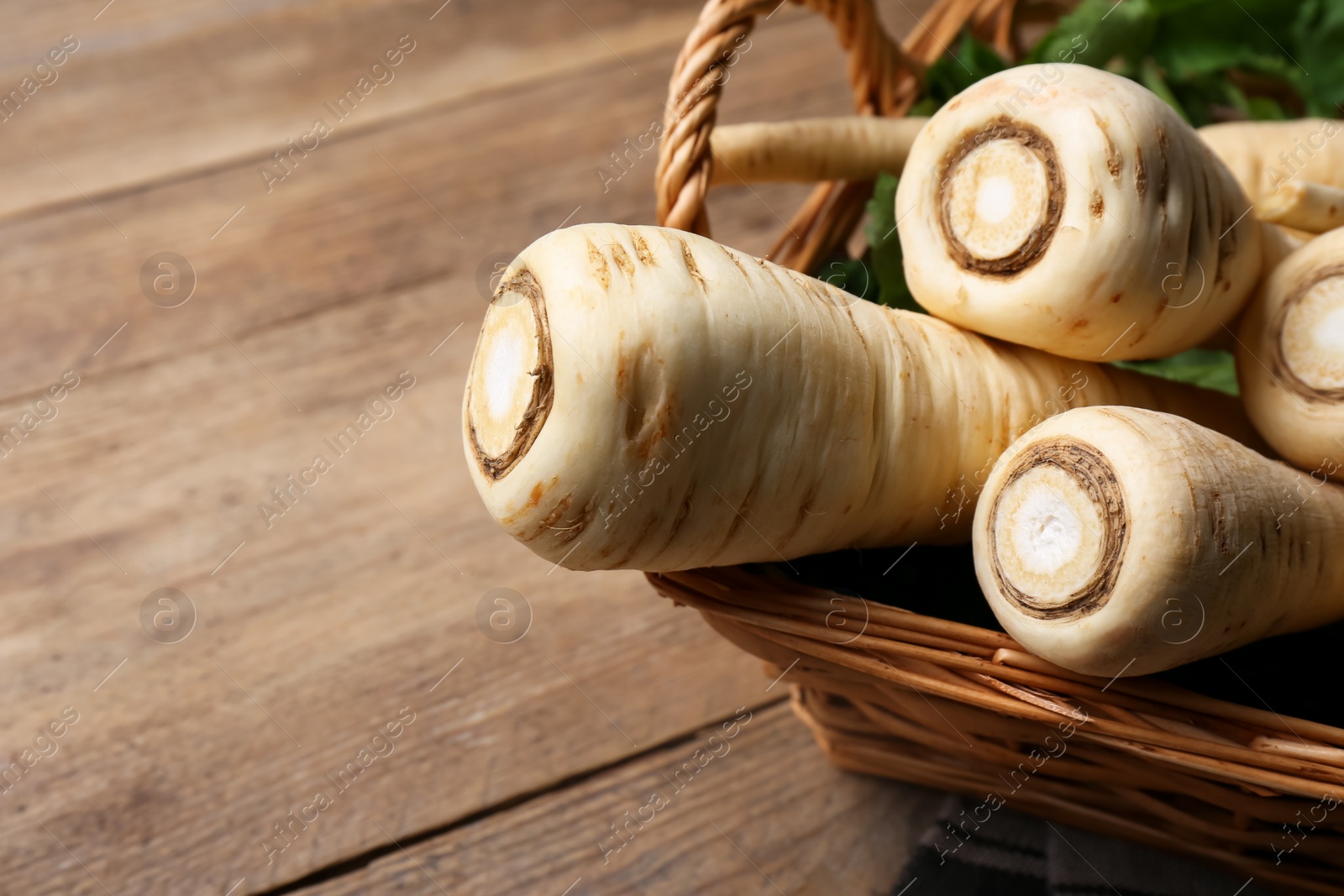 Photo of Wicker basket with delicious fresh ripe parsnips on wooden table, closeup. Space for text