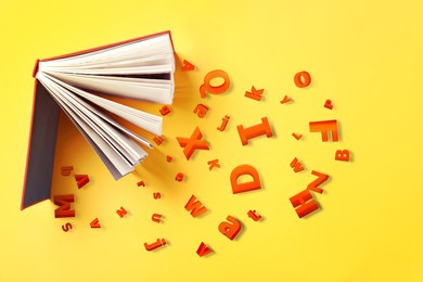 Image of Open book with letters on yellow background, flat lay. Dyslexia concept