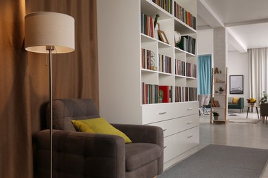 Cozy home library interior with comfortable armchair, floor lamp and collection of books on shelves