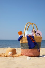 Bag with beach accessories and hat on sand near sea