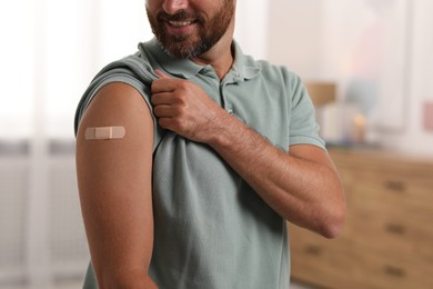 Photo of Man with sticking plaster on arm after vaccination at home, closeup