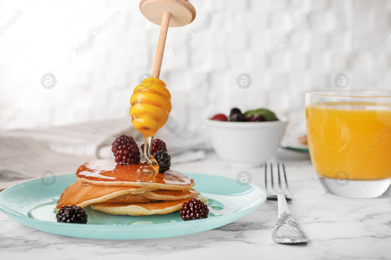 Photo of Pouring honey onto delicious pancakes with berries on table