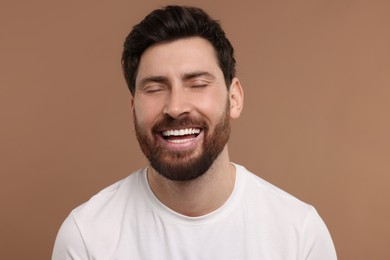 Photo of Handsome man laughing on light brown background, closeup