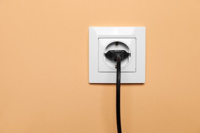 Power socket with inserted plug on pale orange wall. Electrical supply