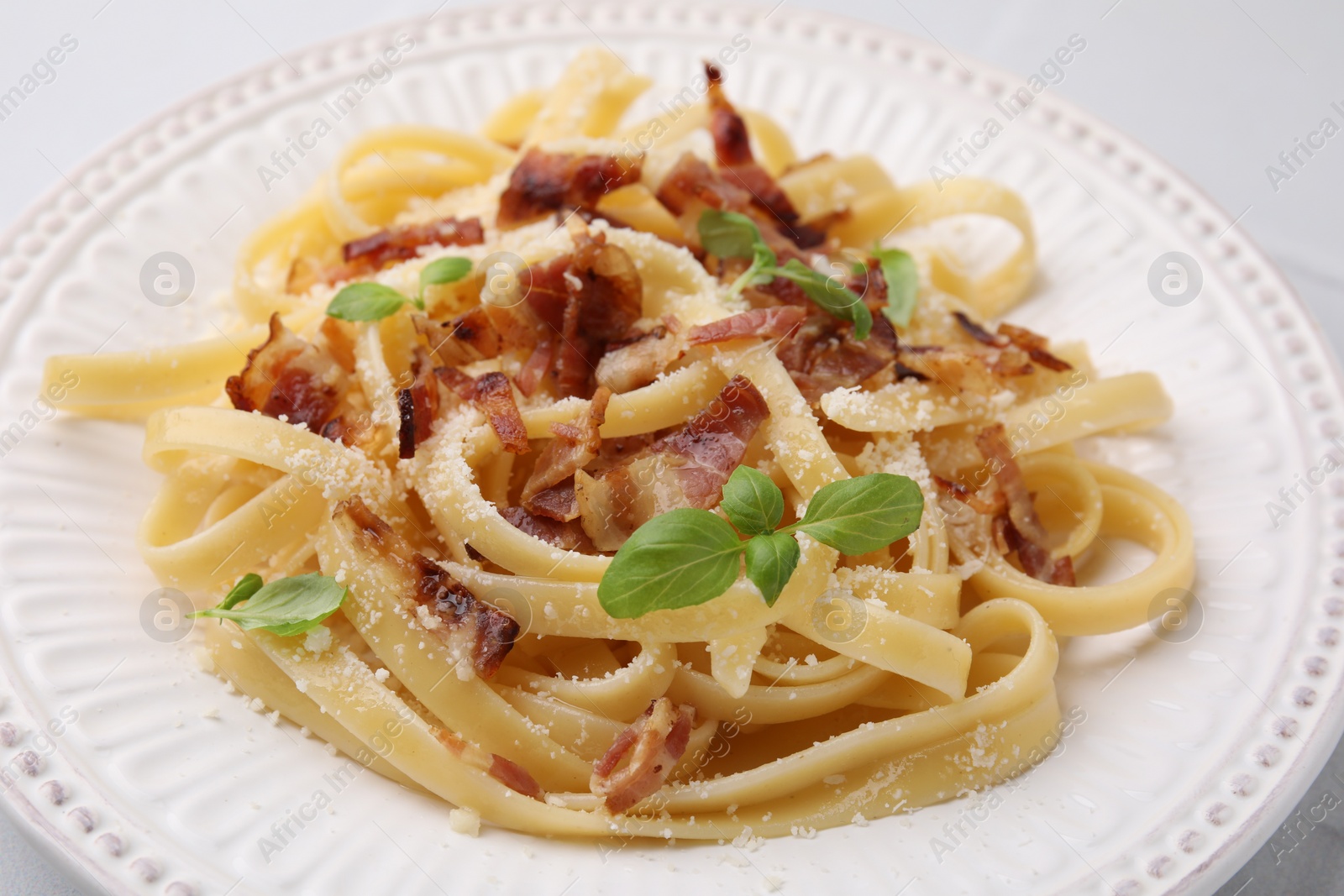 Photo of Tasty pasta with bacon and basil on white table, closeup