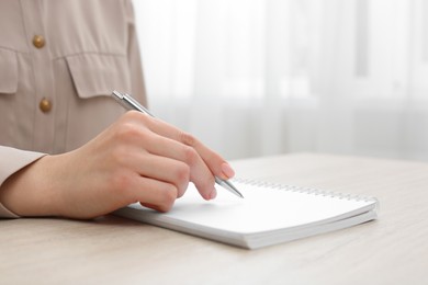 Woman writing in notebook at wooden table, closeup