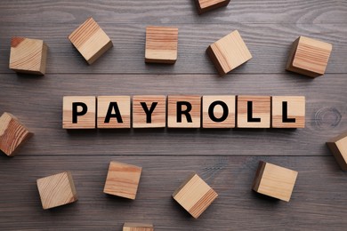 Photo of Cubes with word Payroll on wooden table, flat lay