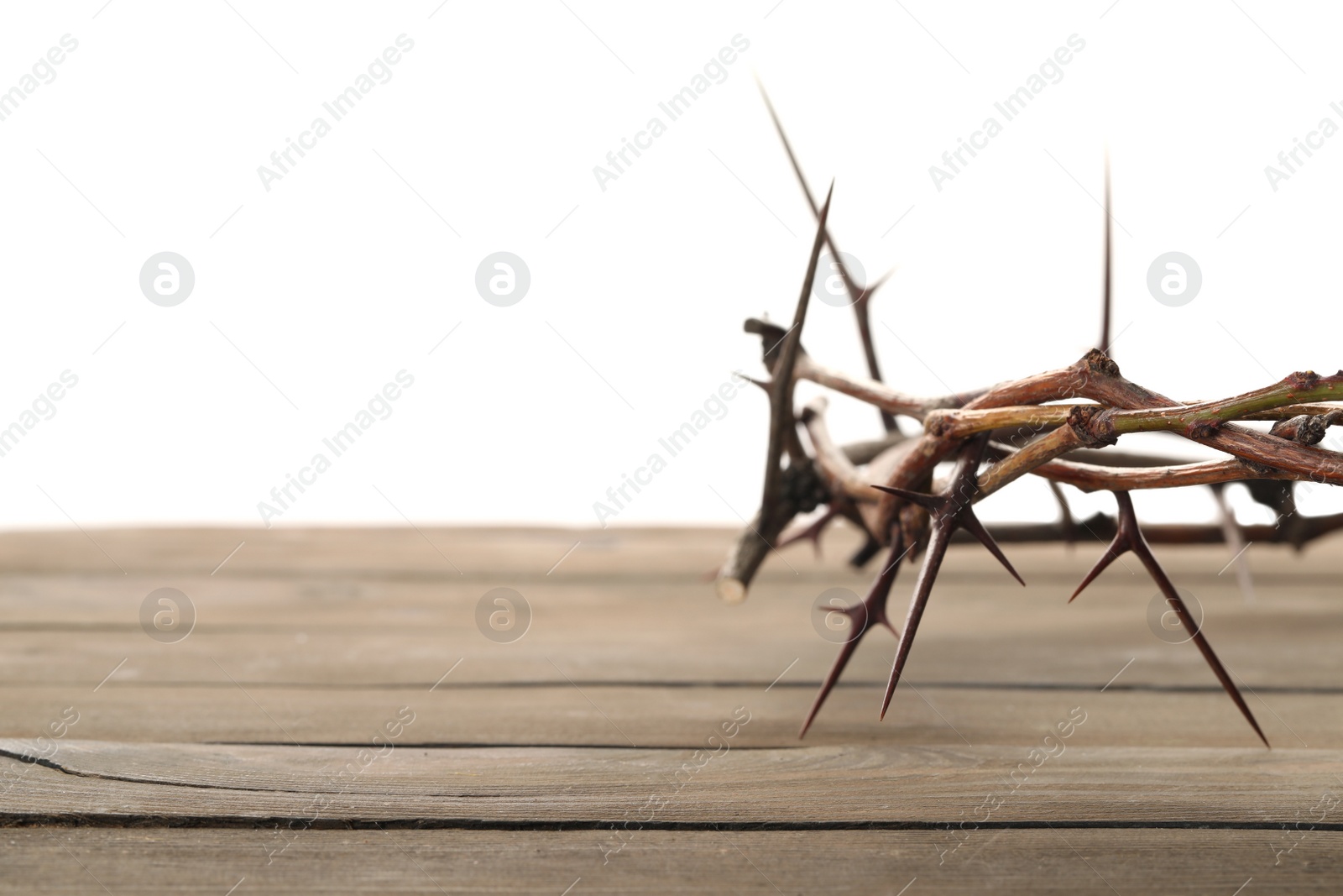 Photo of Crown of thorns on wooden table against white background, closeup with space for text. Easter attribute