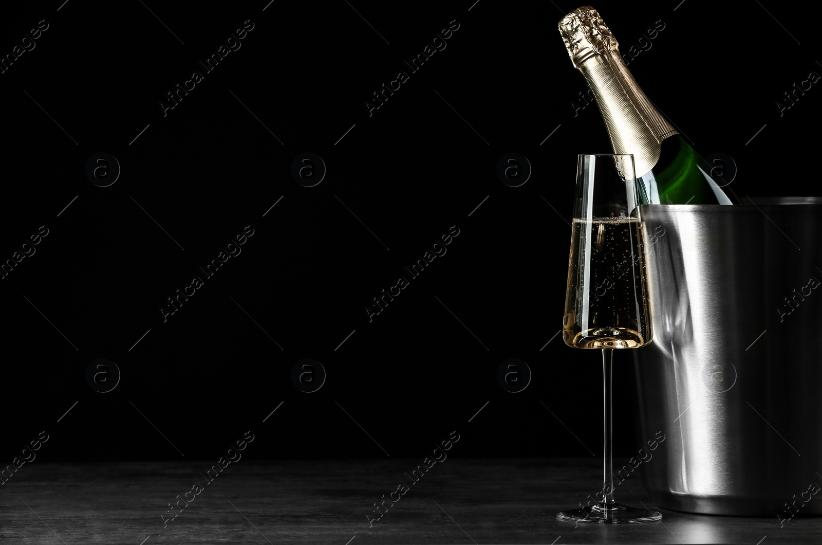 Photo of Glass of champagne near bucket with bottle on black background, space for text