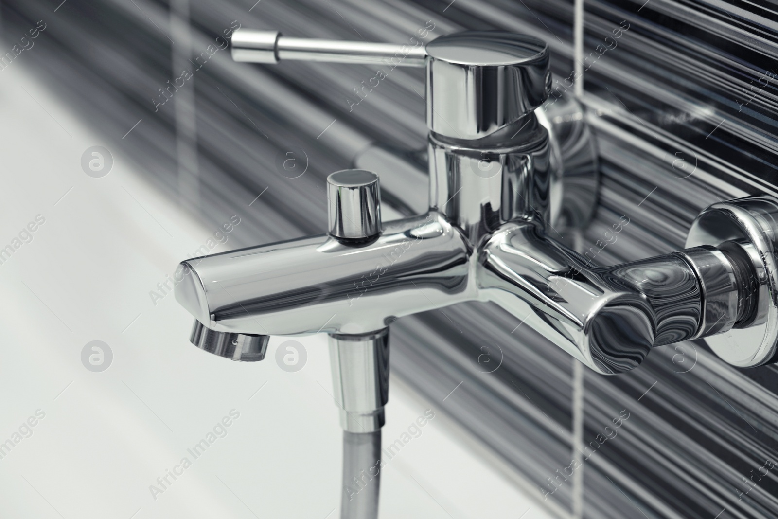 Photo of Shiny bath water tap installed on black and white wall