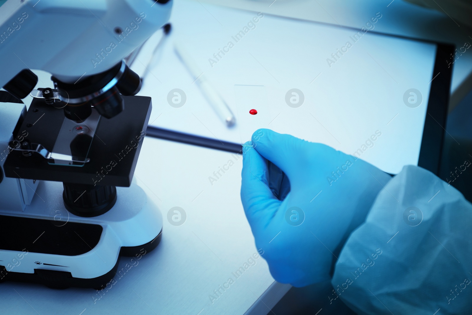 Photo of Scientist in chemical protective suit with blood sample on microscope slide at table, closeup. Virus research