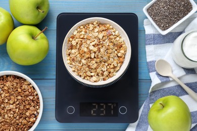 Photo of Electronic scales with granola and different products on light blue wooden table, flat lay