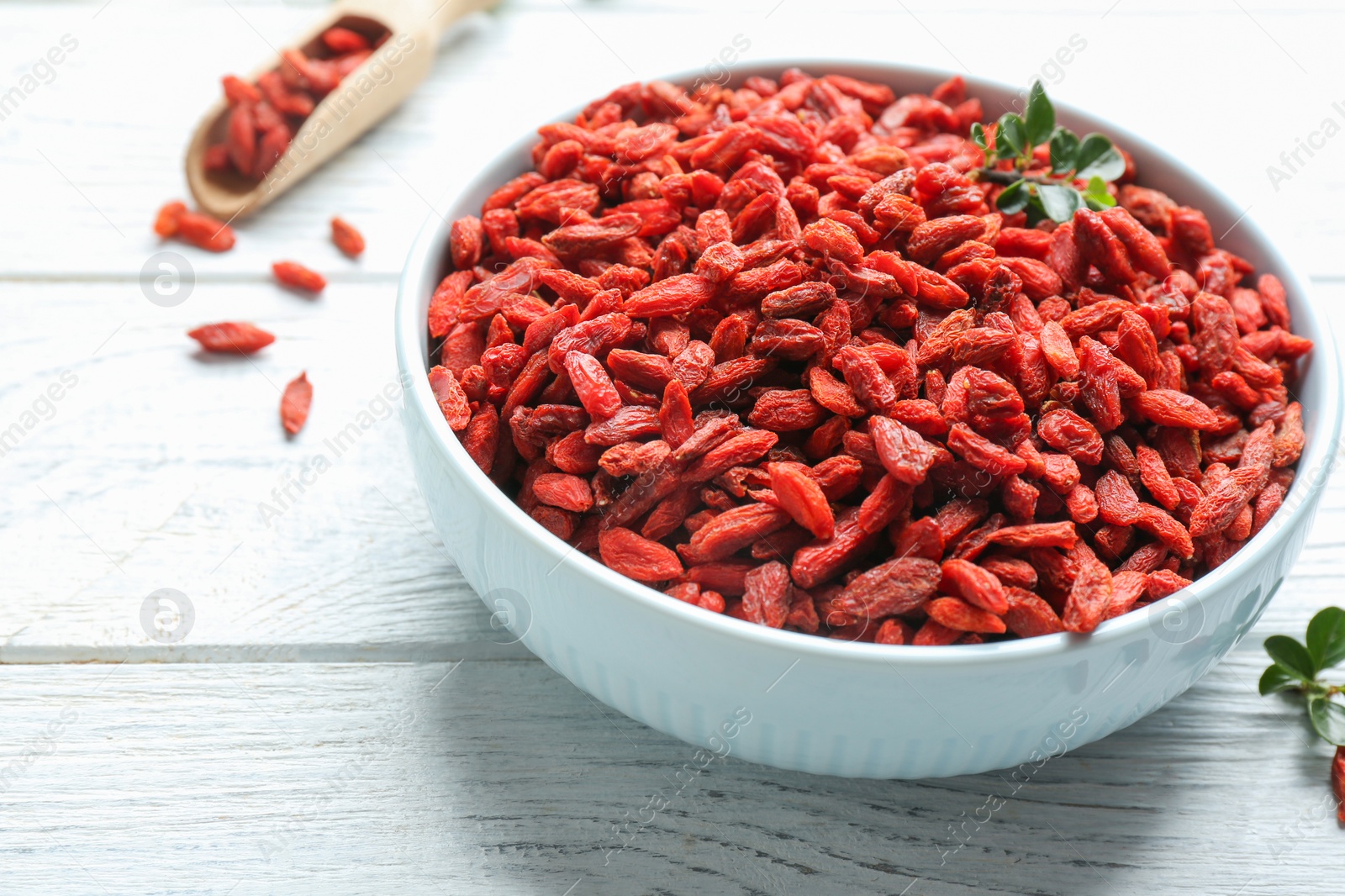 Photo of Bowl of dried goji berries on white wooden table, closeup. Healthy superfood