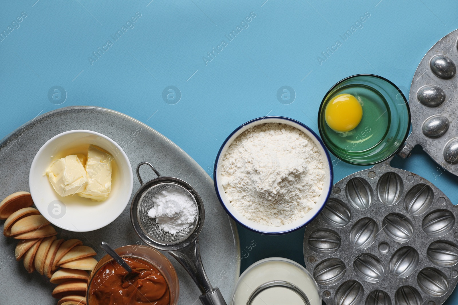 Photo of Baking mold and ingredients for walnut shaped cookies on light blue table, flat lay. Space for text