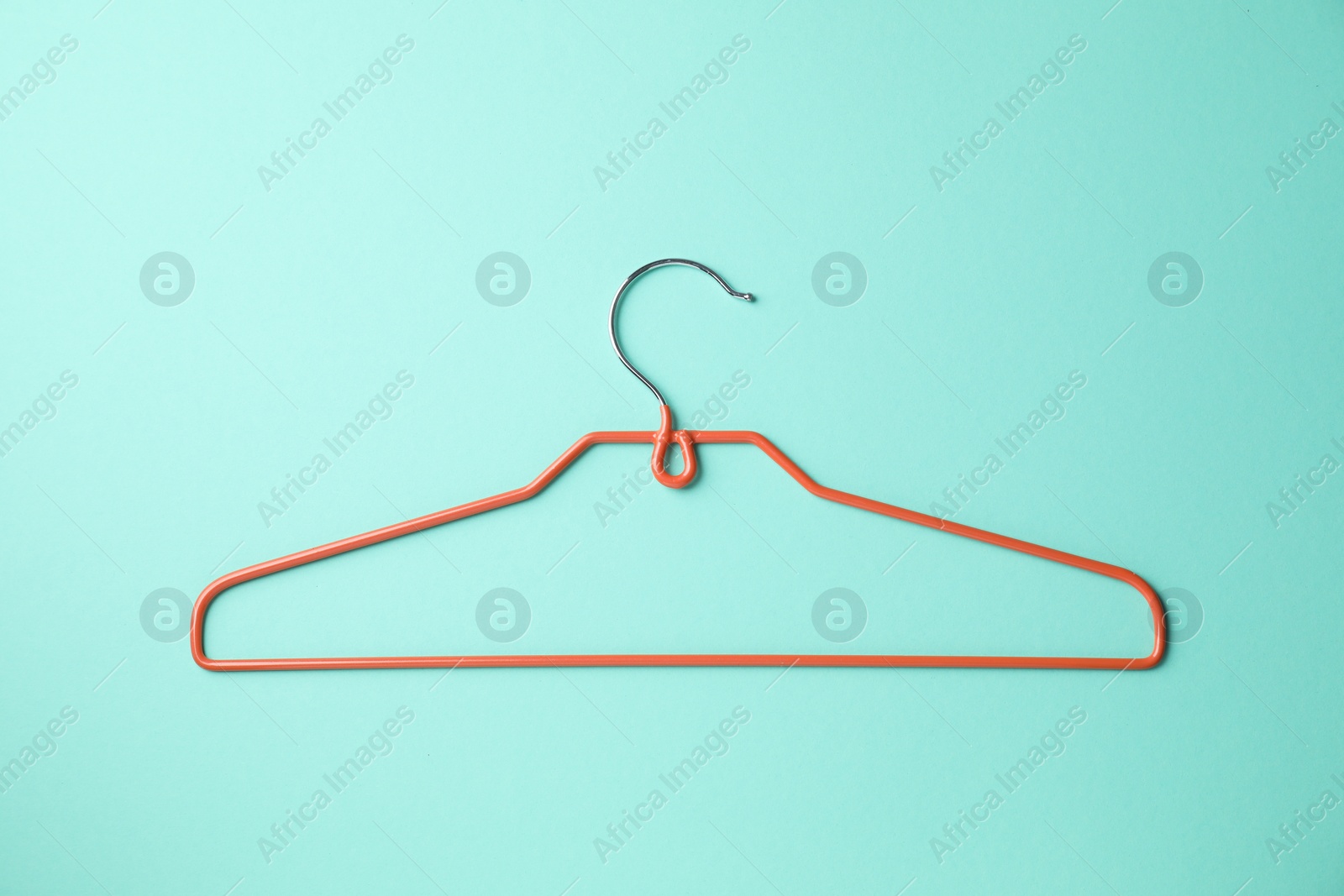 Photo of Empty orange hanger on turquoise background, top view