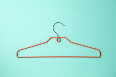 Photo of Empty orange hanger on turquoise background, top view