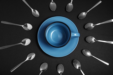 Photo of Flat lay composition with metal spoons and empty cup on black background