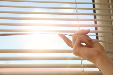 Image of Woman opening window blinds on sunny morning, closeup