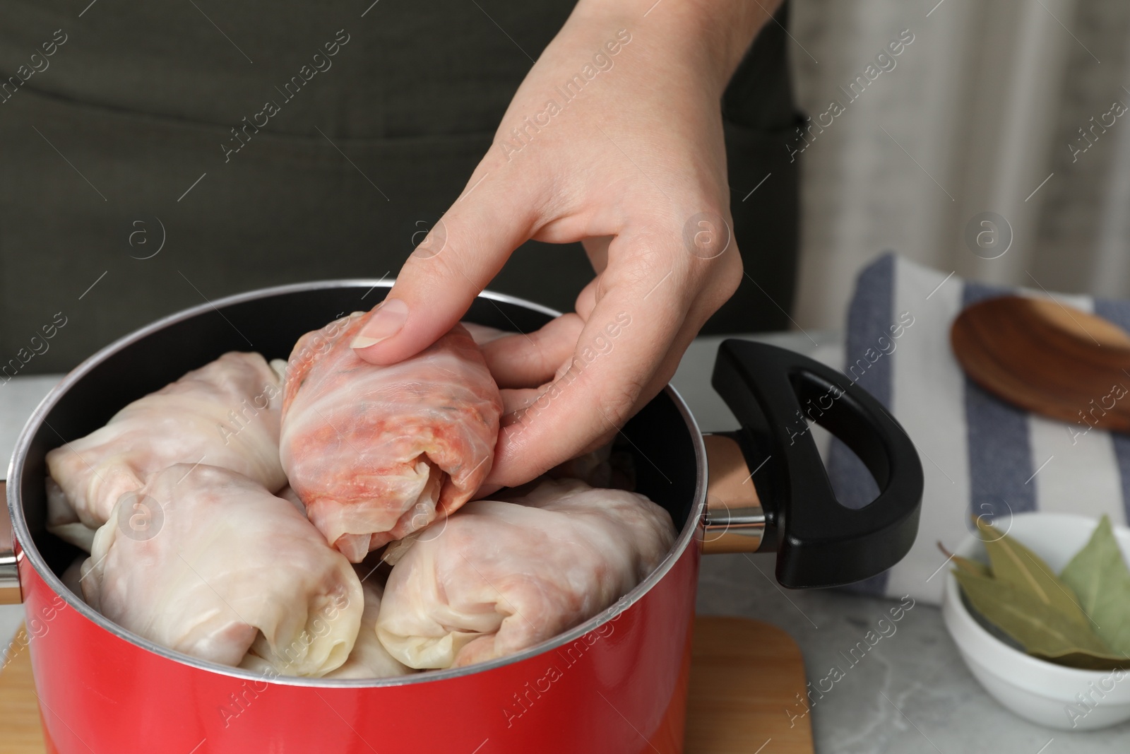 Photo of Woman putting uncooked stuffed cabbage roll into pot at light grey table, closeup