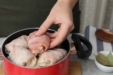 Woman putting uncooked stuffed cabbage roll into pot at light grey table, closeup