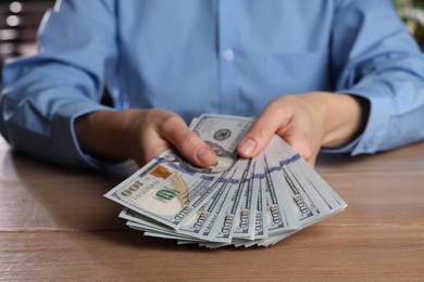 Photo of Money exchange. Woman holding dollar banknotes at wooden table, closeup