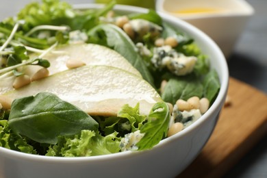 Fresh salad with pear in bowl on table, closeup