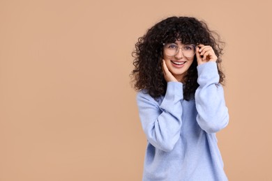 Happy young woman in stylish light blue sweater and glasses on beige background, space for text