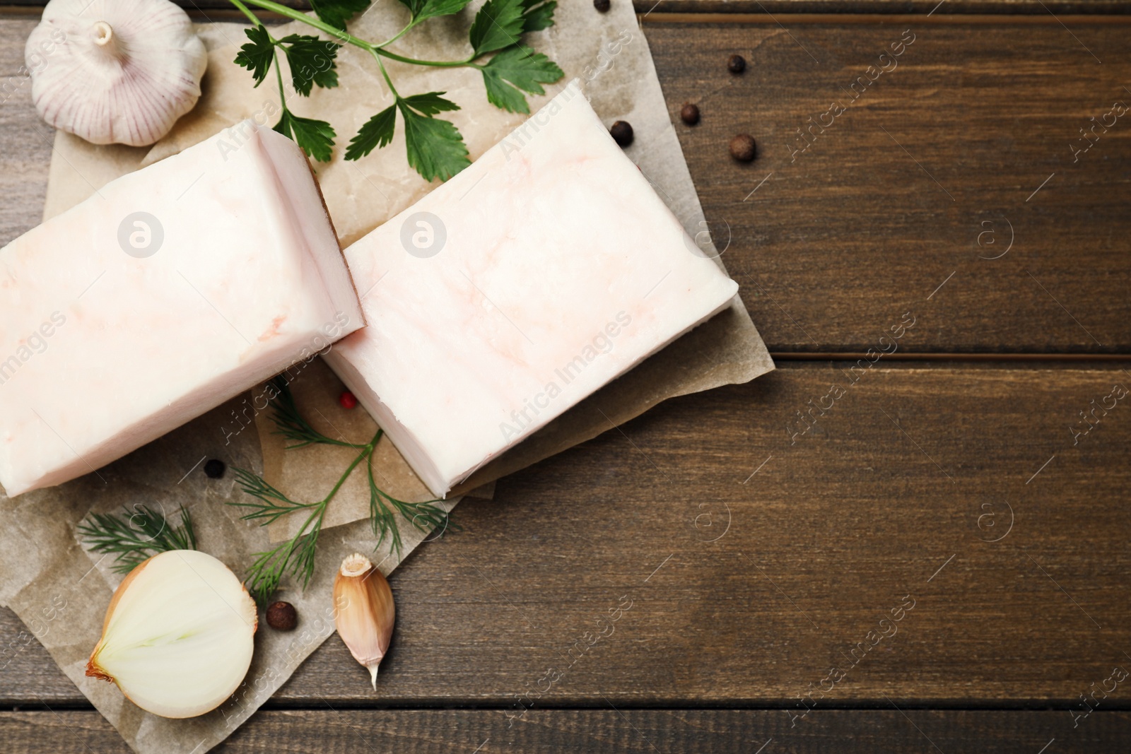 Photo of Tasty salt pork with herbs, onion and garlic on wooden table, flat lay. Space for text