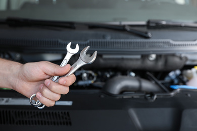 Photo of Professional auto mechanic holding wrenches near modern car in service center, closeup of hand