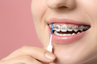 Photo of Smiling woman with dental braces cleaning teeth using interdental brush on pink background, closeup