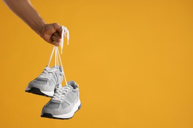 Photo of Man holding stylish sneakers on yellow background, closeup. Space for text