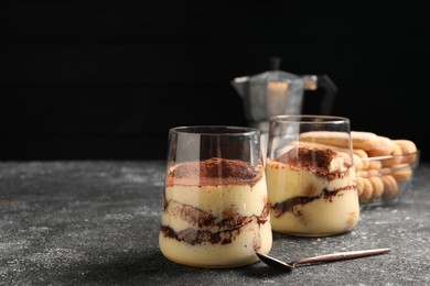 Photo of Delicious tiramisu in glasses and spoon on grey textured table. Space for text