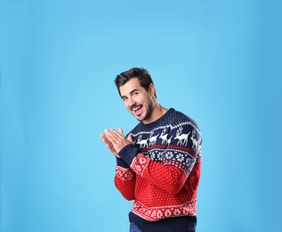 Portrait of happy young man in Christmas sweater on light blue background