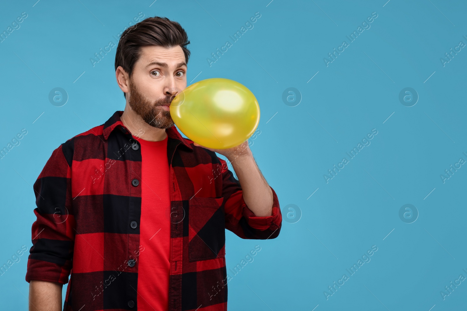 Photo of Man inflating yellow balloon on light blue background. Space for text