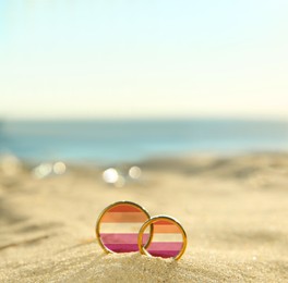 Image of Illustration of lesbian flag and golden wedding rings on sandy beach