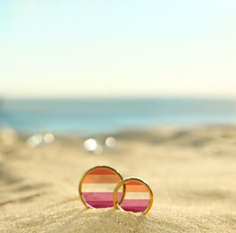 Illustration of lesbian flag and golden wedding rings on sandy beach