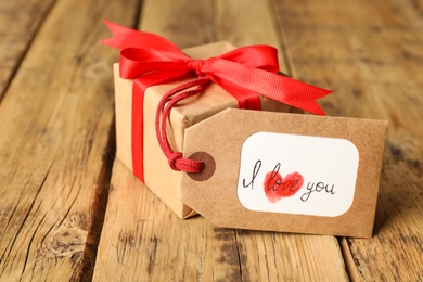 Photo of Tag with text I Love You and gift box on wooden table, closeup