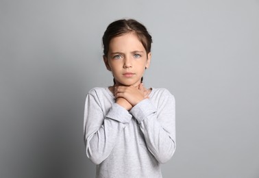 Photo of Little girl suffering from sore throat on grey background