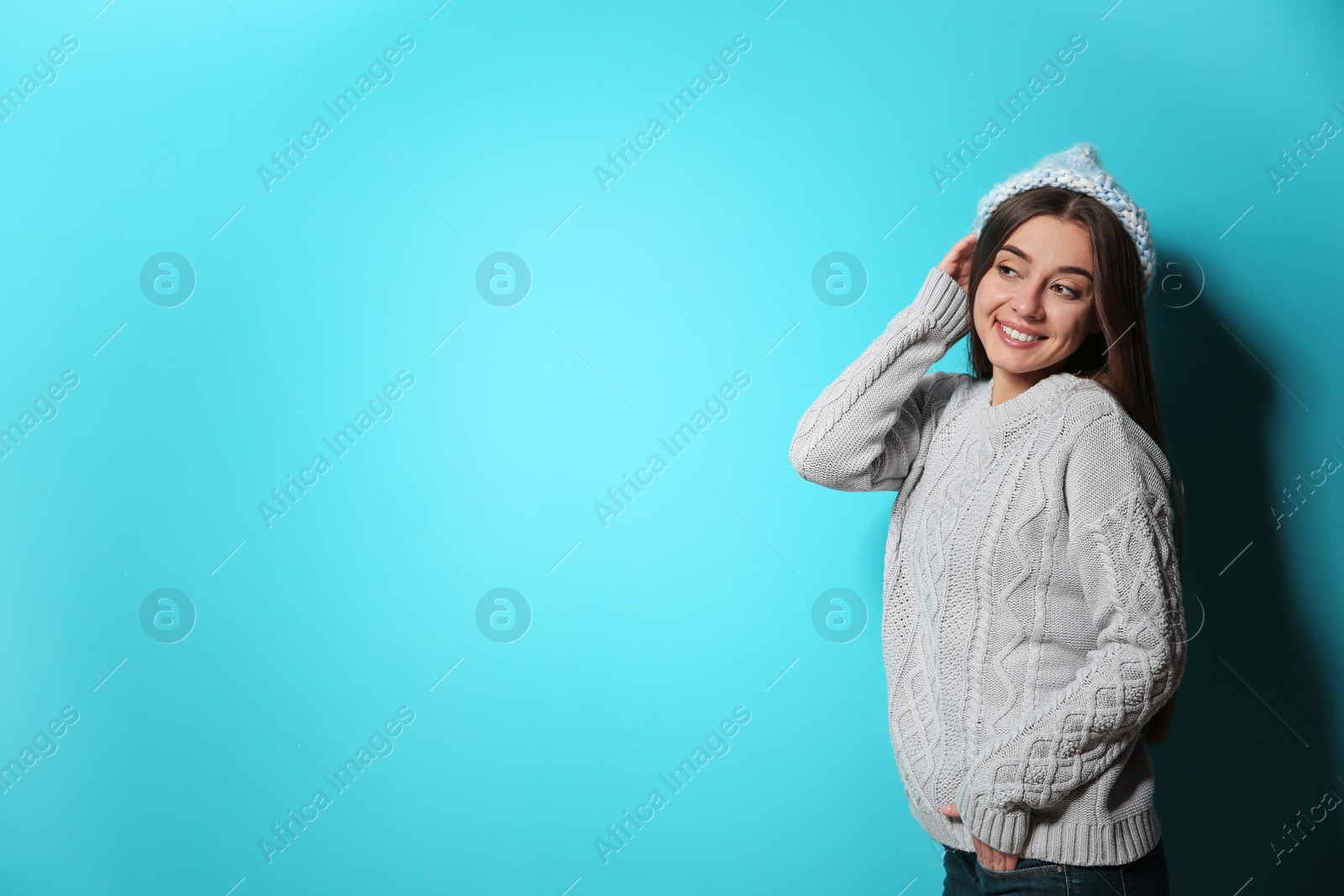 Photo of Beautiful young woman in warm sweater with hat on color background. Space for text